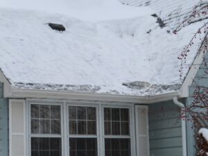 A snow-covered roof over a home's window, with some melting snow and ice accumulation.